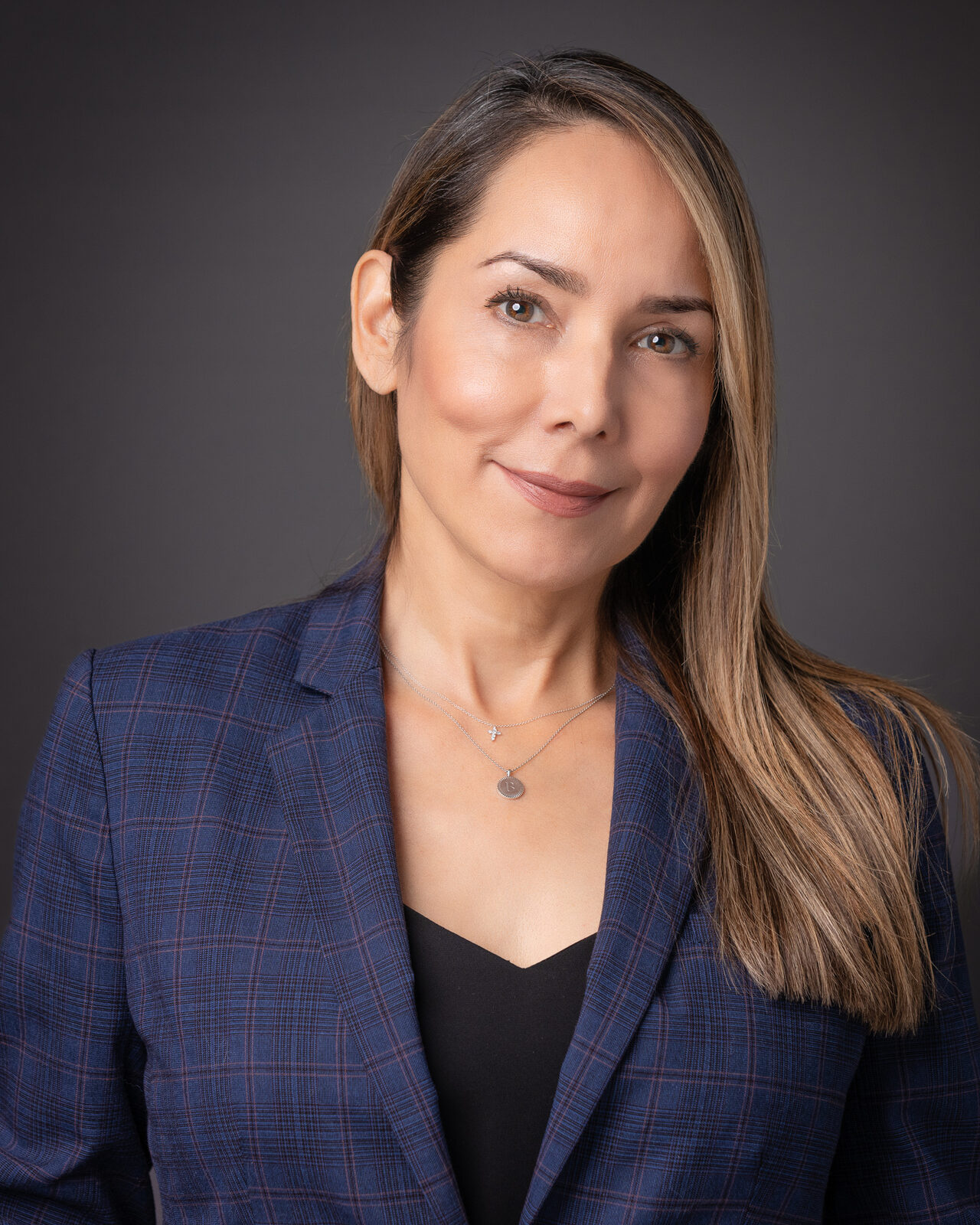 Corporate headshot of a woman in a plaid blazer against a dark background